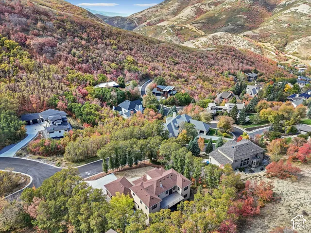 Aerial perspective of a hillside property featuring multi-level rooflines, an attached garage, paved driveway, and substantial surrounding mountain terrain with dense mature vegetation