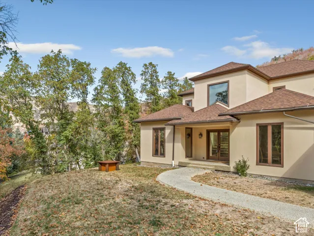 Stucco exterior with a multi-gabled roof, featuring double glass-paned entry doors, custom-fit windows with dark trim, and a concrete paver walkway