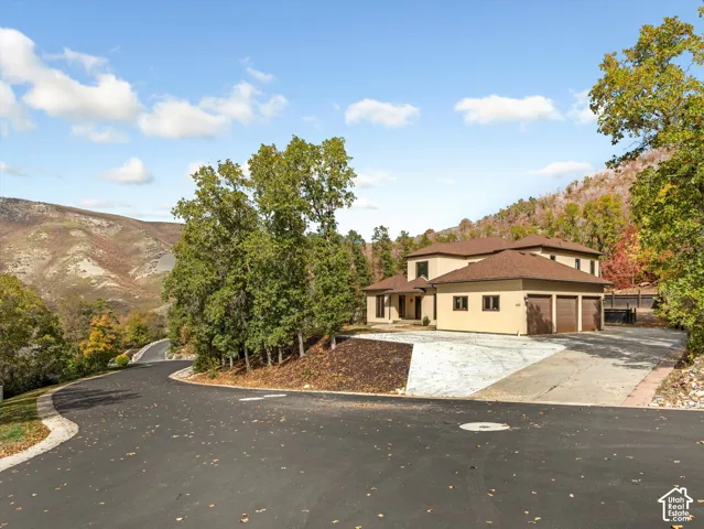 Two-story residence featuring a stucco exterior, three-car garage, concrete driveway, and mountainous topography