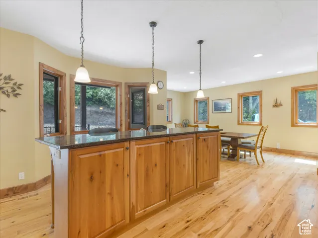 Kitchen island with stone countertop, wood-finish cabinetry, and pendant lighting