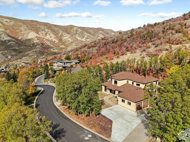 Multi-level residence featuring a brown shingle roof, stucco exterior, concrete driveway, attached multi-car garage, and mountain backdrop