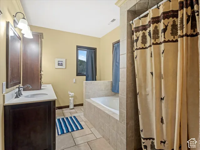 Built-in tub with tile surround, a single vanity with a dark wood-finish cabinet, a single basin sink, and a wall-mounted light fixture