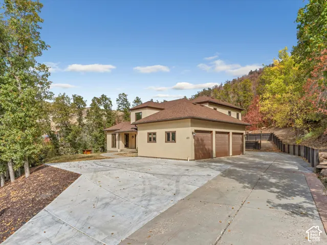 Multi-level stucco exterior with a hip roof, three-car garage, concrete driveway, and natural hillside backdrop