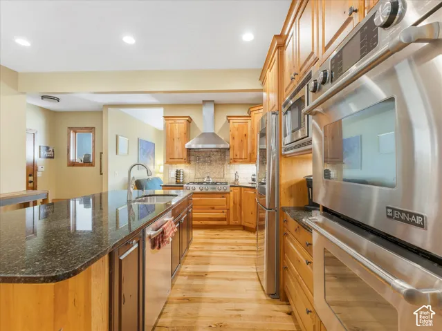 Kitchen featuring wood cabinetry, stainless steel appliances, a center island with an undermount sink, and wood-finish flooring