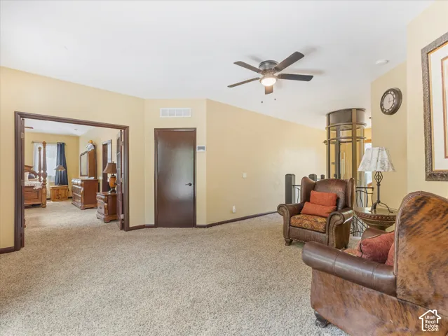 Expansive carpeted area featuring a ceiling fan, a cylindrical residential elevator, a doorway to another room, and a dark wood-finish door