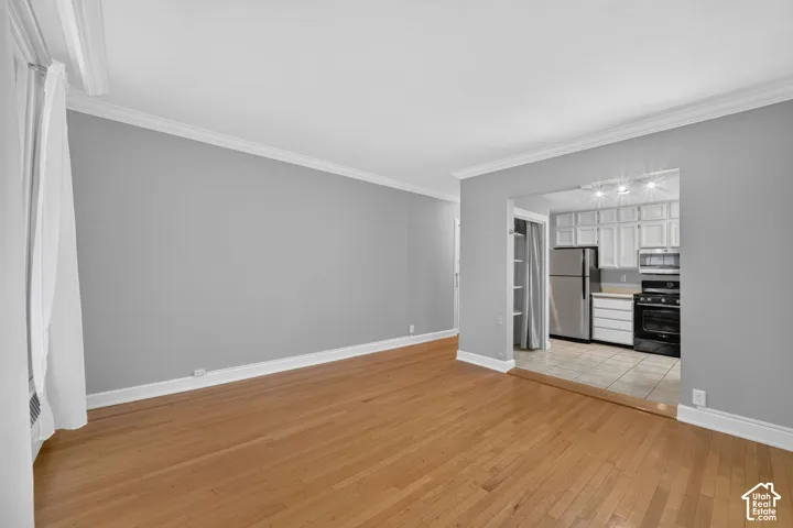 Hardwood flooring, crown molding, a kitchen featuring white cabinetry, stainless steel refrigerator, and a built-in microwave