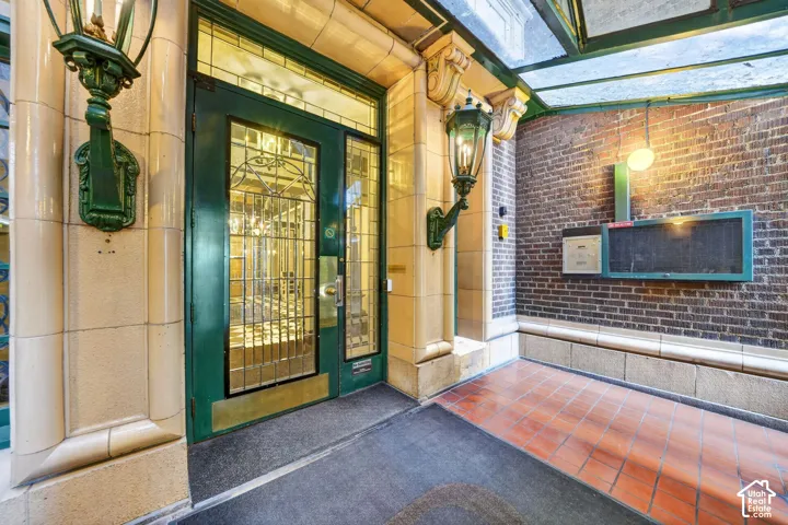 Entryway featuring a green-framed glass door with ornate ironwork, a transom window, and a column with an attached wall sconce
