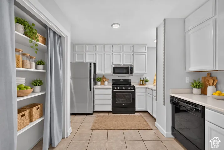 Kitchen with white cabinetry, stainless steel refrigerator, black range, black dishwasher, and tile flooring