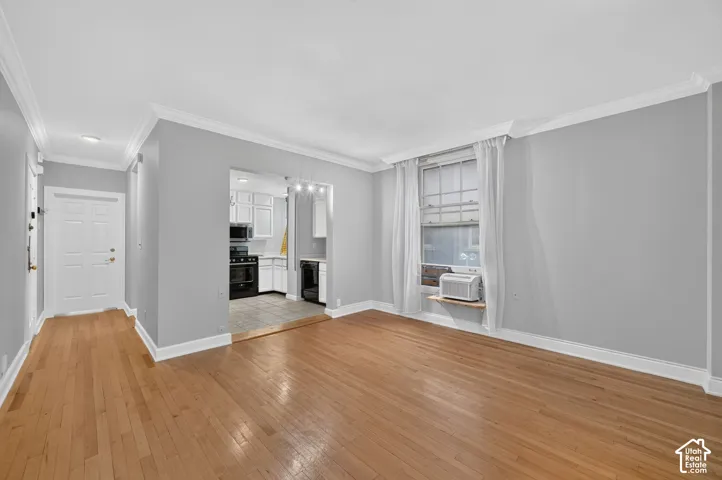 Hardwood flooring, crown molding, white painted door, white window trim, and white kitchen cabinetry