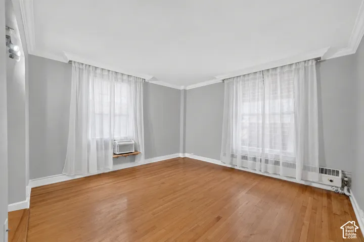 Wood-finish flooring, crown molding, and two windows with sheer privacy treatments