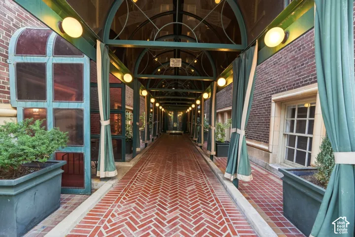 Covered walkway with a herringbone brick pattern, arched metal and glass canopy, spherical wall-mounted lighting, and architectural brick walls