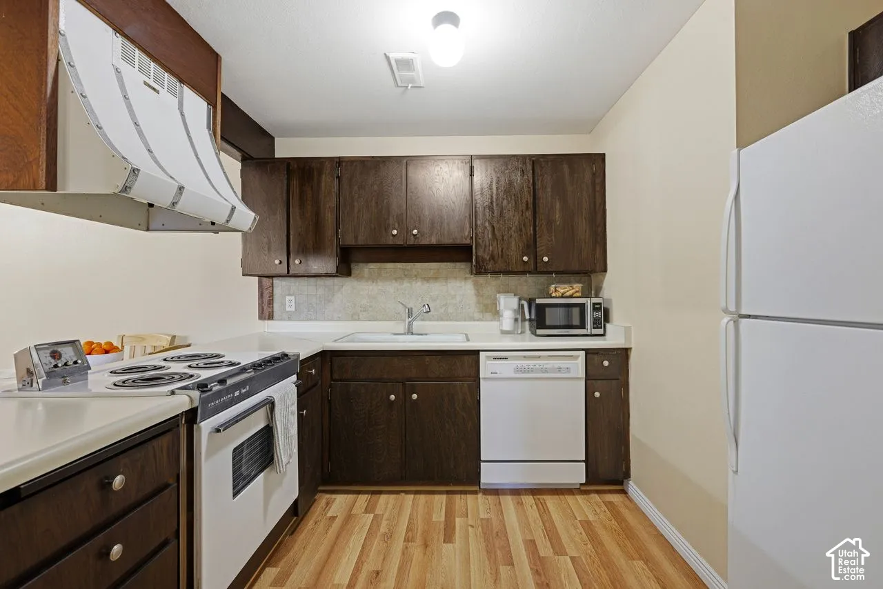 Kitchen featuring wood-finish cabinetry, new laminate flooring, white appliances, and a white countertop