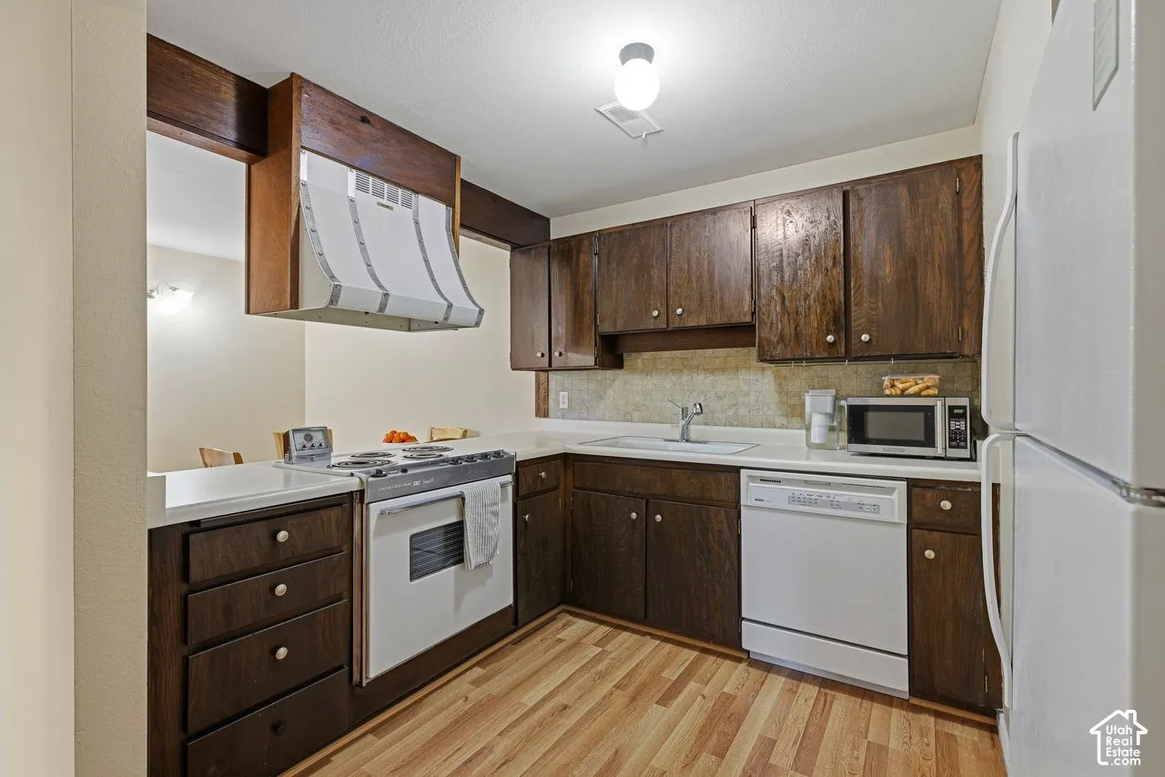 Kitchen featuring new laminate flooring, dark wood cabinetry, white countertops, and a full suite of white appliances