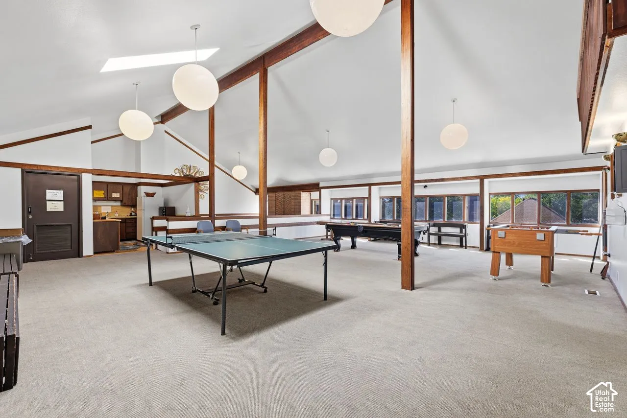 Spacious recreational room featuring vaulted ceilings, exposed wood beams, skylight, and large windows