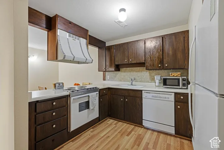 Kitchen featuring new laminate flooring, dark wood cabinetry, white countertops, and a full suite of white appliances