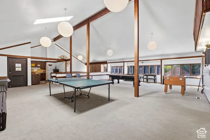 Spacious recreational room featuring vaulted ceilings, exposed wood beams, skylight, and large windows