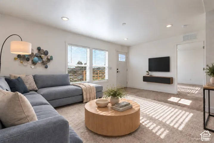 Bright living area with recessed lighting and neutral carpeting