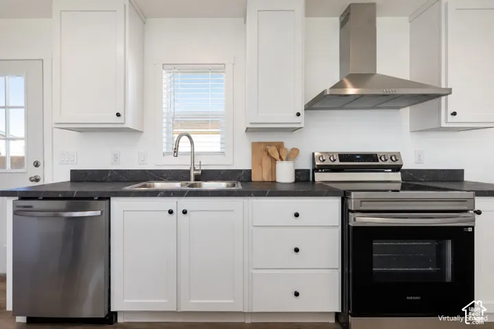 White cabinetry with black hardware, stainless steel appliances, dark countertops, and a stainless steel range hood