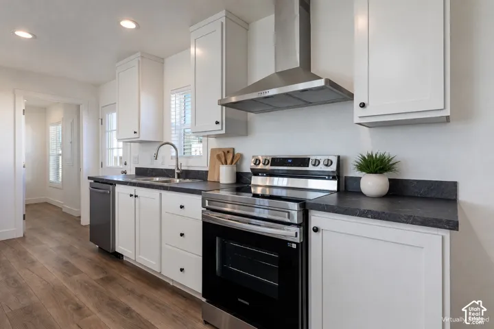 Stainless steel appliances, white cabinetry with black hardware, dark countertops, wood-finish flooring, and recessed lighting