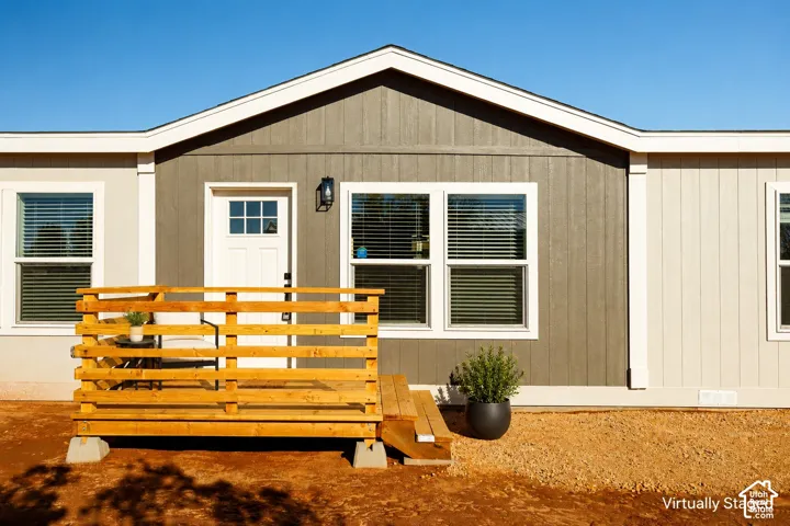 Exterior featuring a wooden deck, a white paneled entry door with windowpanes, and exterior lighting