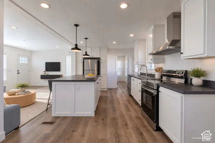 Open-concept kitchen and living area featuring white cabinetry, black countertops, stainless steel appliances including dual wall ovens, pendant lighting, and wood-finish flooring throughout