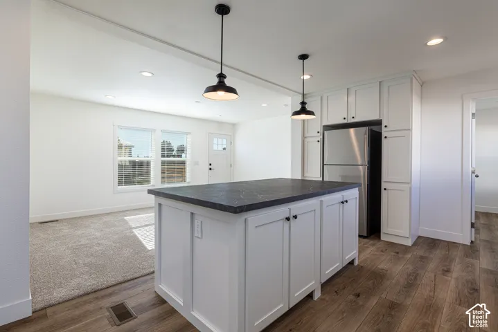 Kitchen island with dark countertop, white shaker cabinetry, stainless steel refrigerator, recessed lighting, and wood-finish flooring