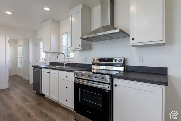 Kitchen featuring stainless steel appliances, dark countertops, white cabinetry with black hardware, and wood-finish flooring