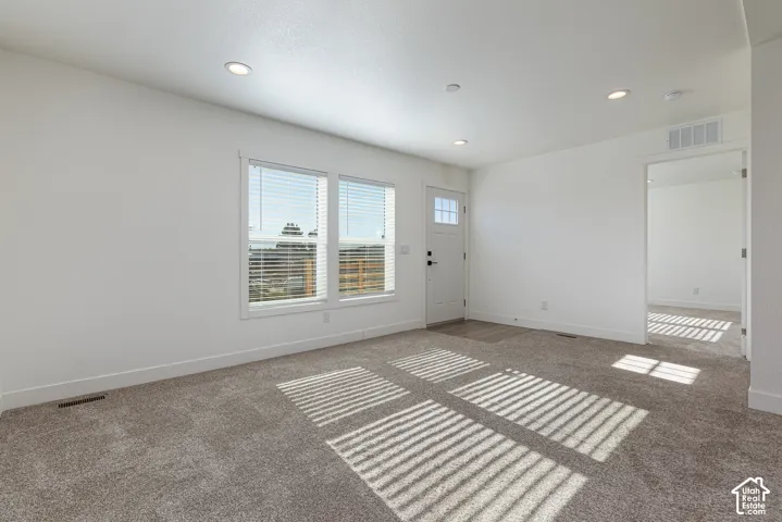 Recessed lighting, white walls, carpet flooring, multiple windows, and a panel door with an integrated window