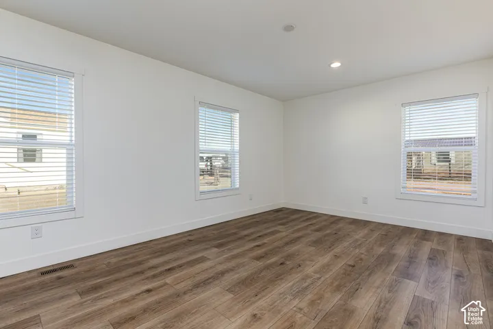 Spacious room featuring wood-finish flooring, white walls, multiple windows with blinds, and recessed lighting
