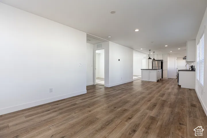 Open-concept living space featuring wood-finish flooring, recessed lighting, and a kitchen with white cabinetry and a central island