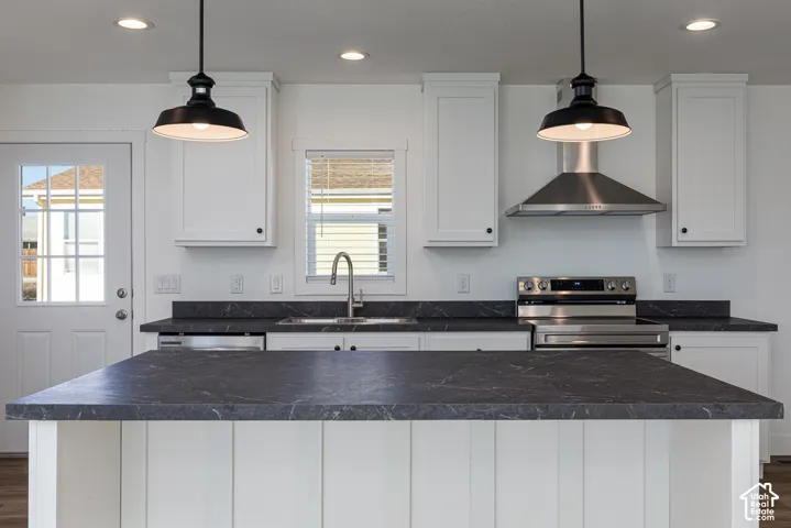 Kitchen featuring white shaker cabinetry, stainless steel appliances, dark stone-finish countertops, and two pendant light fixtures