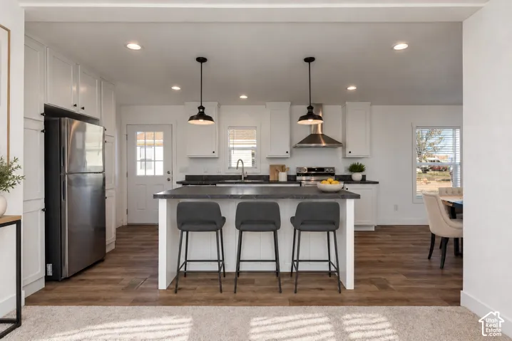 Kitchen featuring white shaker cabinetry, stainless steel appliances, dark countertops, a center island with pendant lighting, and wood-finish flooring