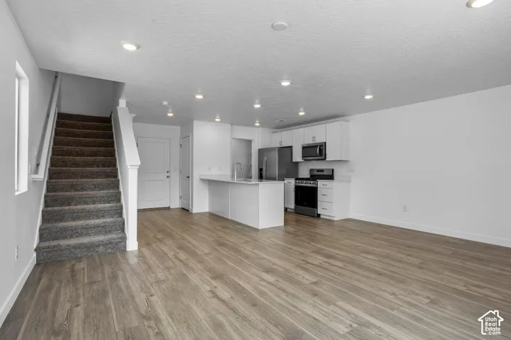 Open-concept living space featuring wood-finish flooring, recessed lighting, and a white kitchen with stainless steel appliances