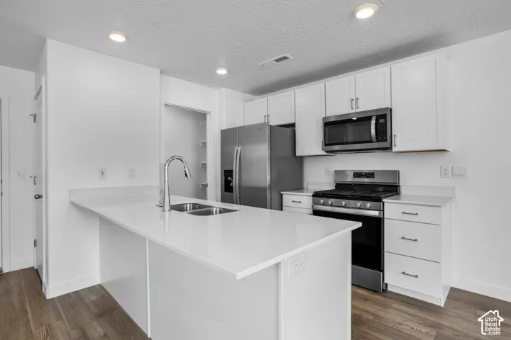 Contemporary kitchen featuring white cabinetry, stainless steel appliances, a center island with sink, white countertops, and wood-finish flooring