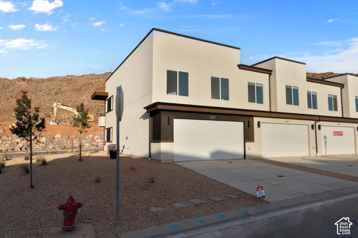 Contemporary townhome exterior with a flat roofline, smooth stucco finish, dark trim accents, and a two-car garage