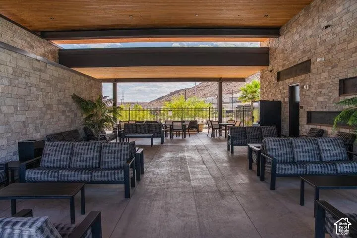 Expansive covered patio with stone accent walls, wood-paneled ceiling, concrete flooring, and built-in linear fireplace