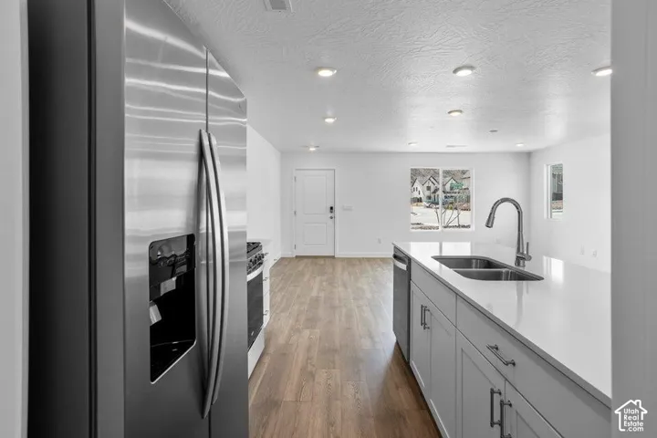 Modern galley kitchen featuring stainless steel French-door refrigerator, black gas range with matching hood, white cabinetry with hardware accents, quartz countertops, undermount sink with contemporary faucet, wood-finish flooring, and recessed ceiling l