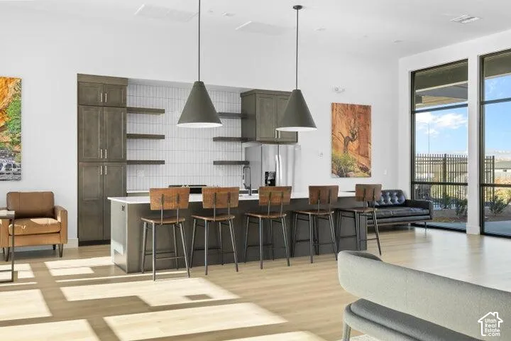 Open-concept living area featuring wood-finish flooring, a kitchen island with seating, a full-height tile backsplash, and extensive window panels