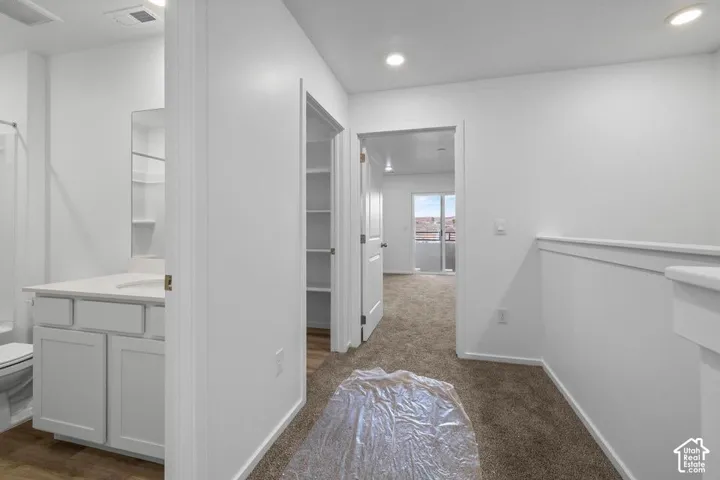 White vanity with a single sink and quartz countertop, built-in shelving, and carpeting throughout