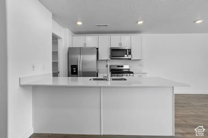 Modern kitchen featuring white cabinetry, stainless steel appliances including a refrigerator, gas cooktop, and microwave, quartz countertops with waterfall edge detailing, and wood-finish flooring throughout