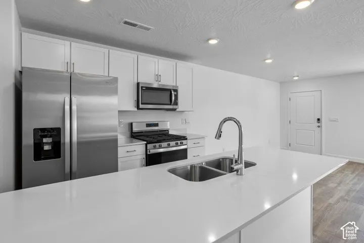 Kitchen featuring stainless steel appliances, white cabinetry, a dual basin sink with a gooseneck faucet, and light-toned countertops
