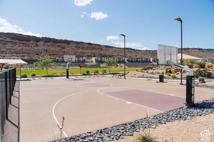 Outdoor sports court with two basketball hoops, integrated lighting, fenced perimeter, and landscaped rock and grass areas