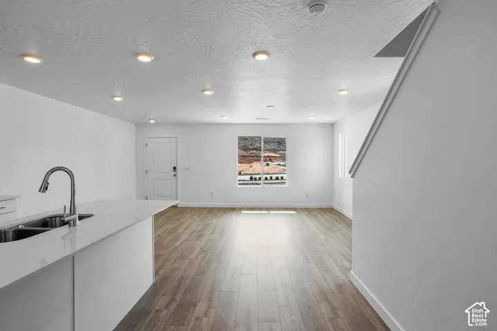 Open-concept living space with recessed lighting, wood-finish flooring, and a kitchen island featuring an integrated double-basin sink and a pulldown faucet