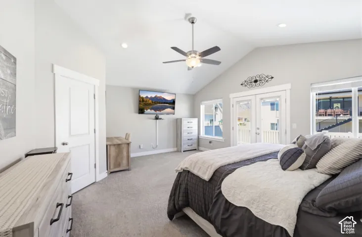 Primary bedroom featuring vaulted ceilings with ceiling fan and integrated lighting, plush carpeting, dual French doors opening to exterior spaces, built-in cabinetry, and abundant natural light from multiple windows