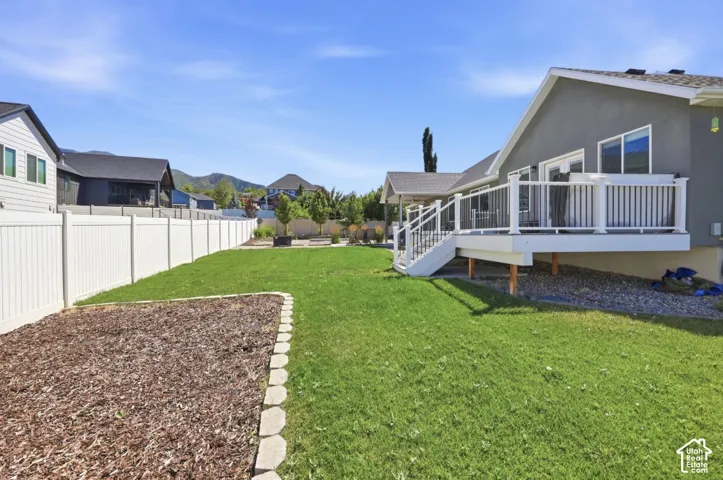 Expansive backyard featuring a manicured lawn, white privacy fencing, and a raised composite deck with white railings
