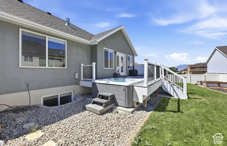 Deck with white railings and an integrated hot tub, stucco exterior, gravel landscaping, and a manicured lawn