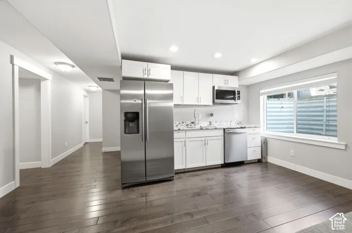 Kitchenette featuring white cabinetry, stainless steel appliances, speckled countertops, and wood-finish flooring