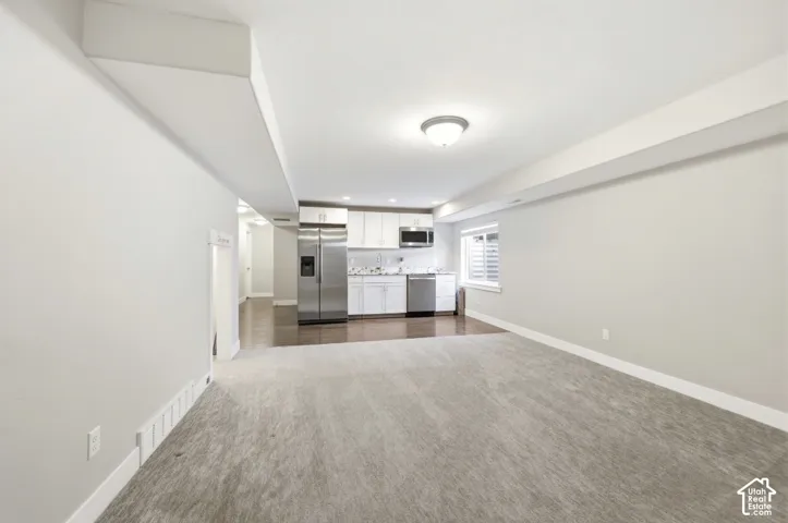Open-concept living area featuring a kitchen with white cabinetry, stainless steel appliances, wood-finish flooring, and a carpeted lounge space