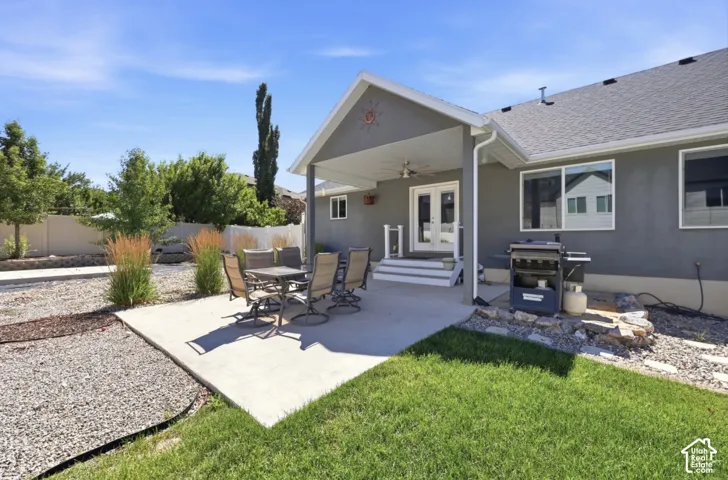 Covered patio with a ceiling fan, concrete patio, double exterior doors, and a manicured lawn