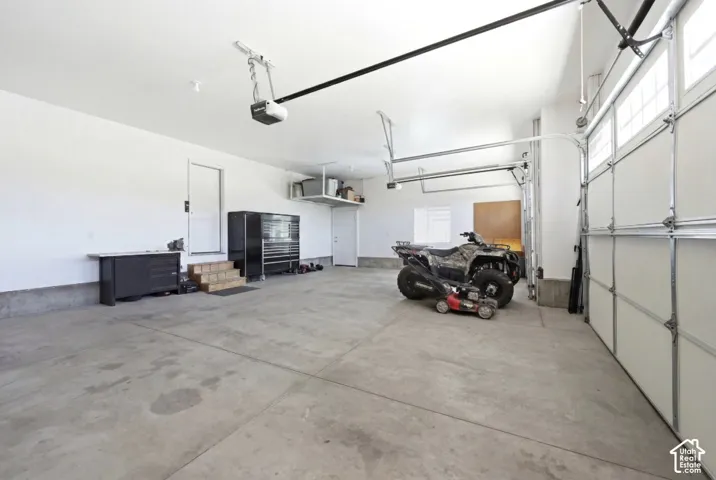 Concrete flooring in a spacious garage with white walls, overhead storage, and dual garage door openers
